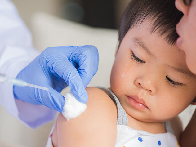 Doctor giving an injection vaccine to a girl. Little girl crying with her mother on background